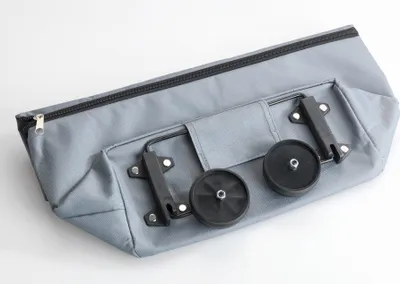 A gray fabric shopping bag with wheels and a handle, lying on a white surface.