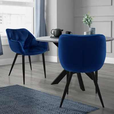 Two dark blue velvet dining chairs are shown around a round dining table in a dining room setting.