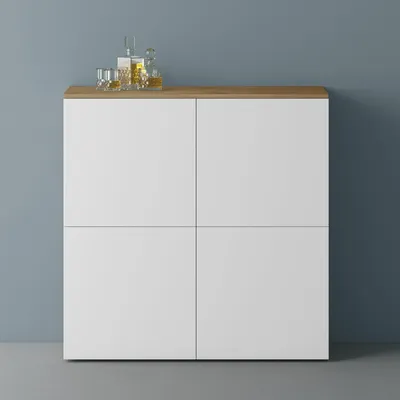 A white cabinet with a wooden top is shown against a blue wall and gray floor. There are two glasses and a bottle of liquor on top of the cabinet.