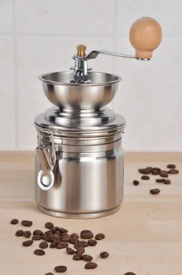 A manual coffee grinder with coffee beans on a wooden surface.