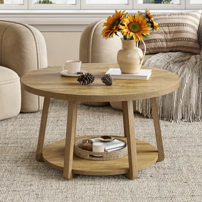 A round wooden coffee table with a two-tiered shelf, decorated with sunflowers in a vase, pinecones, and a cup of coffee.