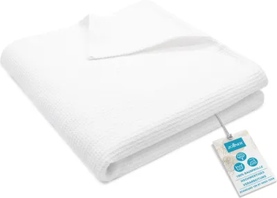 A folded white waffle pique blanket with a product tag attached.