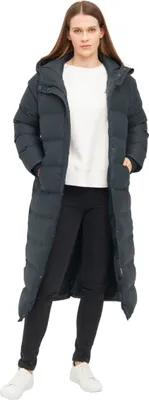 A woman wearing a long, dark gray puffer coat and black pants stands against a white background.