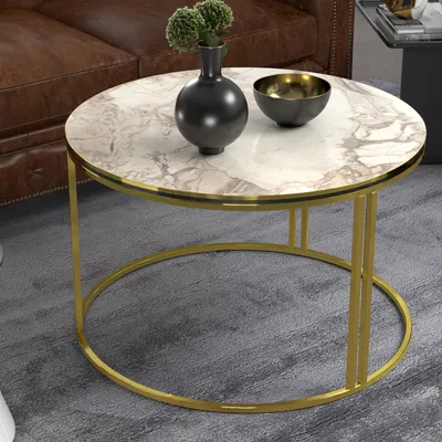 A round coffee table with a marble top and gold metal legs, placed on a gray carpet next to a brown leather sofa. Decorative items are on the table.