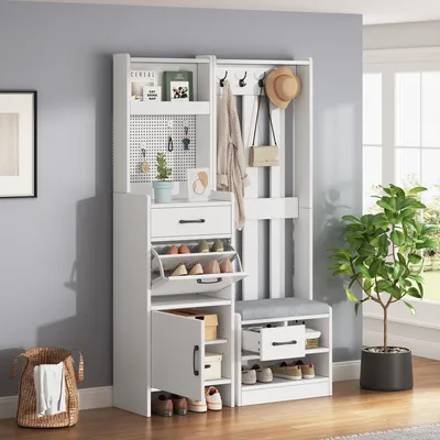 A white entryway organizer with a bench, shelves, drawers, and hooks, set against a light gray wall and a window with greenery outside.
