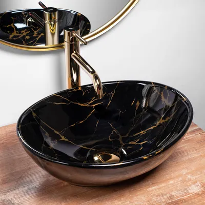 A black marble basin with gold accents and a gold faucet is shown on a wooden surface, with a gold-rimmed mirror in the background.