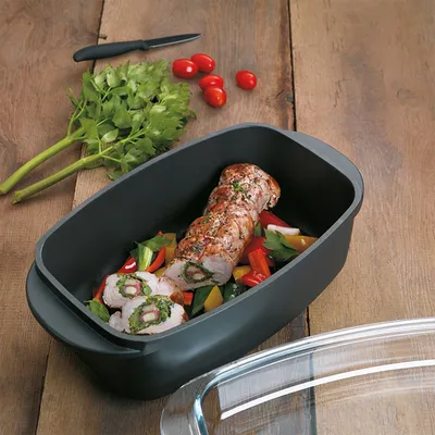 A roasted meat roulade with vegetables in a roasting pan, with parsley and cherry tomatoes on the side.
