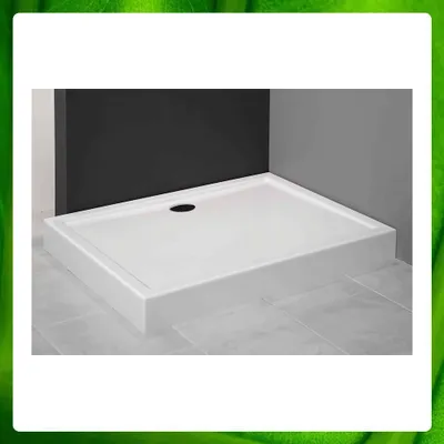 A white shower tray with a drain hole is shown in a corner of a bathroom, with dark gray and black walls behind it.