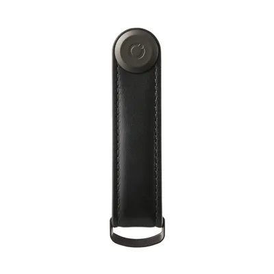 A black leather key organizer with a dark gray circular logo on top and a metal loop at the bottom, isolated on a white background.