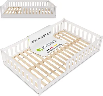 A white wooden children's bed frame with a slatted base, shown from a slightly elevated angle. A label is placed on the bed base.