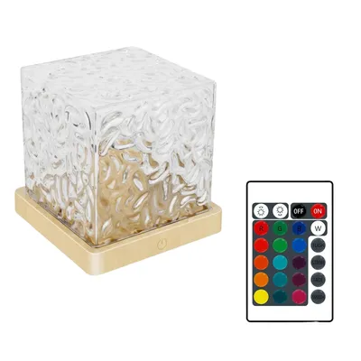 A cube-shaped lamp with a textured glass shade sits on a gold base, next to a remote control.
