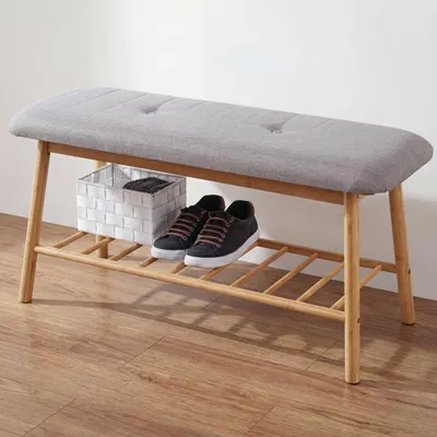 A bench with a shoe rack underneath, with shoes and a basket on it.