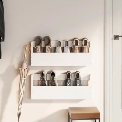 Two white wall-mounted shoe shelves with shoes and an umbrella are displayed on a light gray wall next to a white door.
