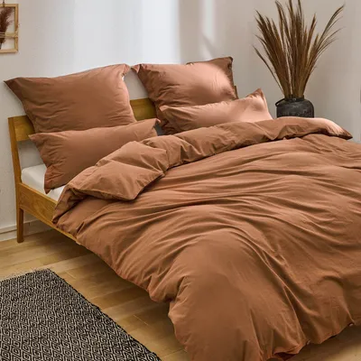 A neatly made bed with brown bedding and pillows, set against a white wall.