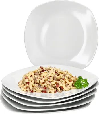 A stack of white square plates with one plate in the foreground filled with pasta and garnished with parsley.