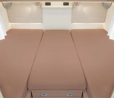 Interior view of a campervan or caravan with three beds made up with fitted sheets.