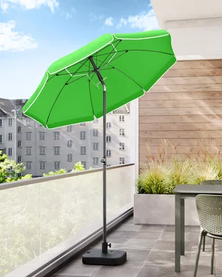 A green patio umbrella is set up on a balcony with a table and chairs.