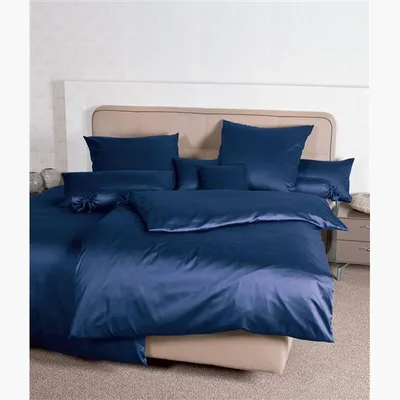 A neatly made bed with navy blue satin bedding and several pillows.