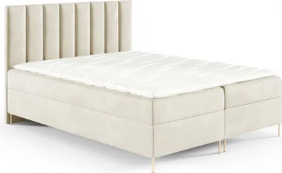 A beige upholstered boxspring bed with a fluted headboard and gold legs, shown against a white background.