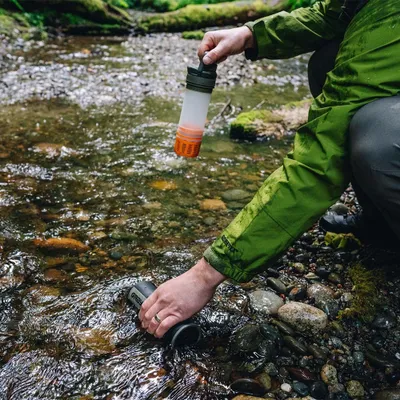 A person is using a water purifier bottle in a stream.