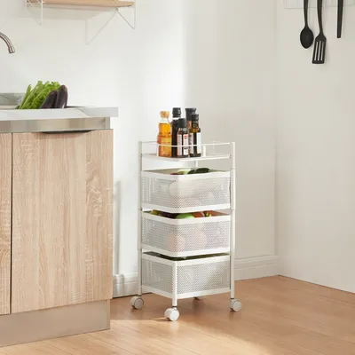 A white rolling cart with three mesh baskets filled with produce and bottles of oil on top, placed next to a kitchen counter.