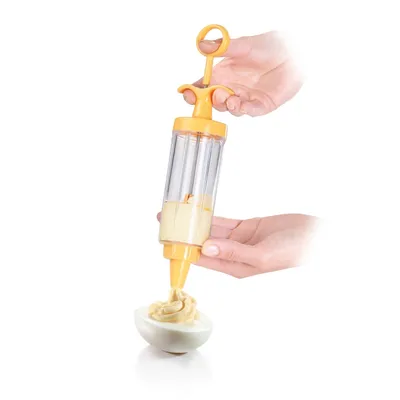Hands are holding a yellow and clear decorating syringe, filling a deviled egg with a creamy filling.