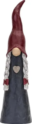 A gnome figurine with a red hat, gray braids, and a dark blue dress with a heart emblem.