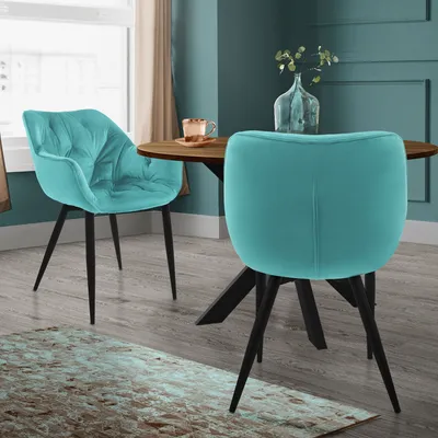 Two teal dining chairs are shown in a dining room setting with a wooden table.