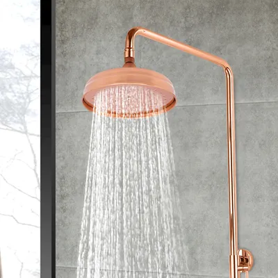 A close-up of a copper shower head with water spraying from it, set against a gray tiled wall.