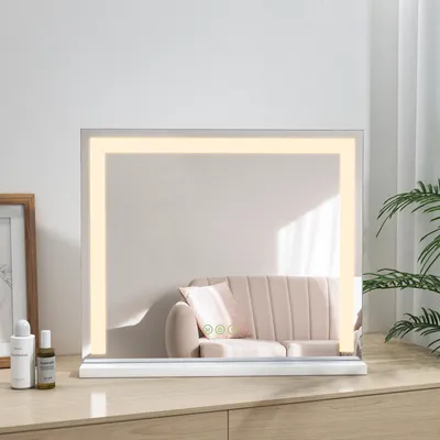 A lighted makeup mirror sits on a wooden dresser, reflecting a sofa and a plant.