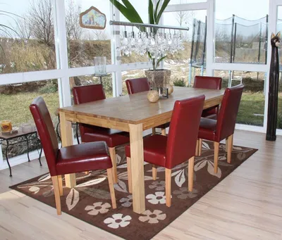 A dining table with red chairs in a sunroom with a view of a backyard.