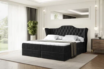 A bedroom scene with a large black upholstered bed as the main focus, set against a backdrop of sheer curtains and a large mirror.