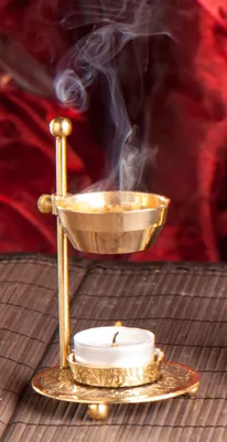 A brass incense burner with smoke rising from it, set against a red fabric background and a brown mat.