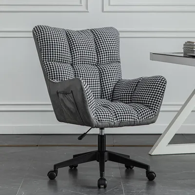 A close-up shot of a computer chair with a houndstooth pattern, placed on a dark tiled floor in front of a white paneled wall.