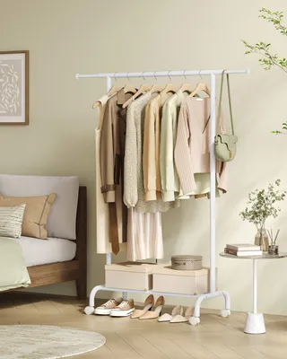 A white garment rack with clothes and accessories is placed next to a bed in a bedroom.
