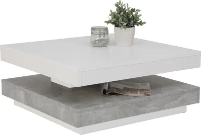 A square coffee table with two tiers, one white and one gray with a concrete-like texture, is shown against a white background. A small potted plant and a glass jar with decorative stones are on the top tier, and a magazine is on the bottom tier.
