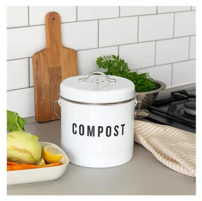 A kitchen counter with a compost bin, vegetables, and a cutting board.