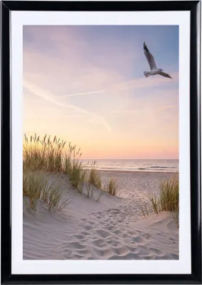 A framed picture of a beach scene with a seagull flying in the sky at sunset.