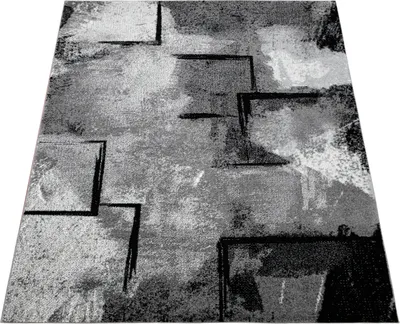 A rug with a modern abstract geometric pattern in shades of gray, black, and white, shown from a slightly elevated diagonal angle.