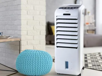 A white air cooler is placed in a modern living room next to a blue pouf.