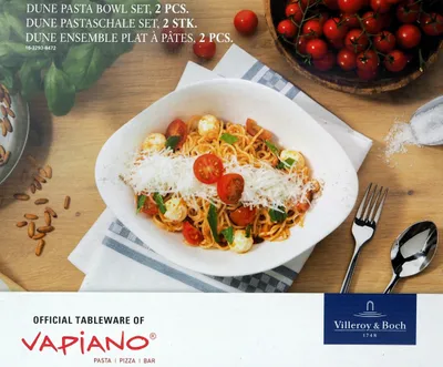 A bowl of pasta with tomatoes and mozzarella, served with cutlery on a wooden table.