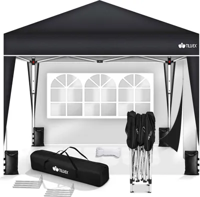 A black pop-up gazebo with its frame, carrying bag, and accessories laid out in front of a white wall with a decorative window.