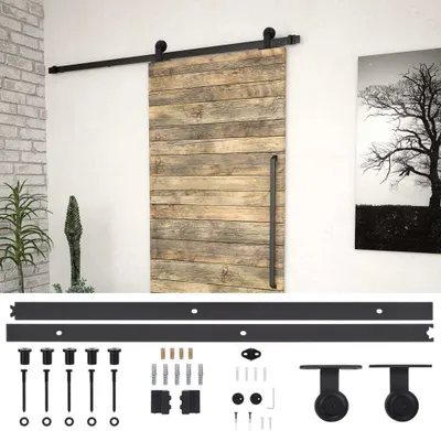 A sliding barn door with a black metal track and hardware, displayed against a white wall with a framed picture of a tree and a plant in a pot.