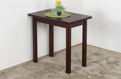 A dark brown wooden table with a green placemat and a small vase of yellow flowers on top, placed in a corner against a white wall and on a beige carpet.