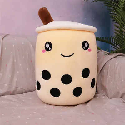 A plush toy bubble tea is placed on a bed with pillows and a plant in the background.