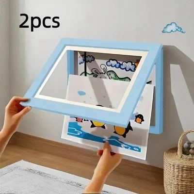 Hands are shown inserting artwork into a light blue picture frame mounted on a wall.