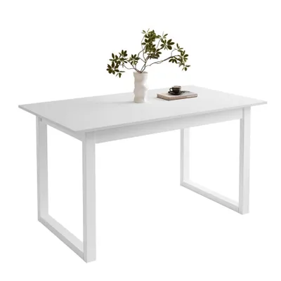 A white dining table with a vase of greenery and a book on top, set against a white background.