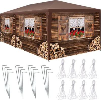 A brown gazebo with a printed image of a wooden chalet, including windows with curtains and flower boxes, and stacks of firewood. Below the gazebo are metal stakes and ropes, likely for assembly or securing the gazebo.