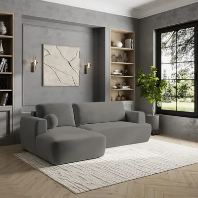 A modern living room with a grey sectional sofa, bookshelves, and a large window.