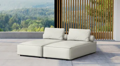 A cream-colored double chaise lounge is placed on a patio with a scenic view of a forest in the background.